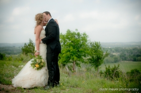 A bride wearing a Vera Wang wedding gown and her groom kissing at a hilltop wedding in the Texas hill country.