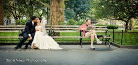 An Indian wedding couple spontaneously kisses on a park bench in New York City sitting next to a man reading a newspaper in Madison Square Park.